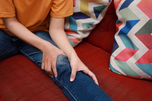 特写照片中，亚洲女子正坐在沙发上，抱着自己的腿，膝盖关节疼痛图片下载