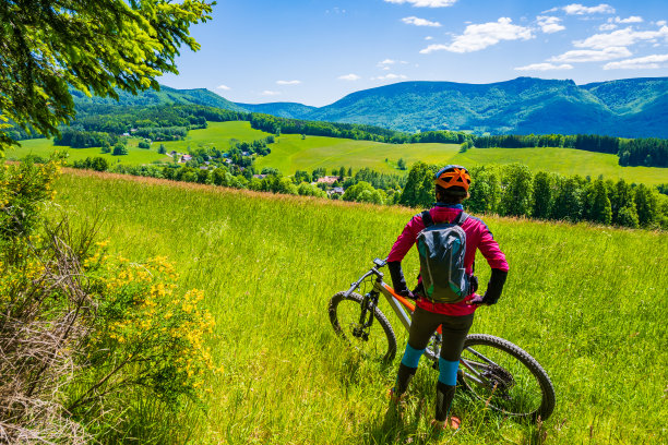 在捷克共和国斯姆姆的斯格列特克，骑山地车的女子背着背包，在吉泽拉山脉绿色山丘之间的单轨小路上休息图片下载