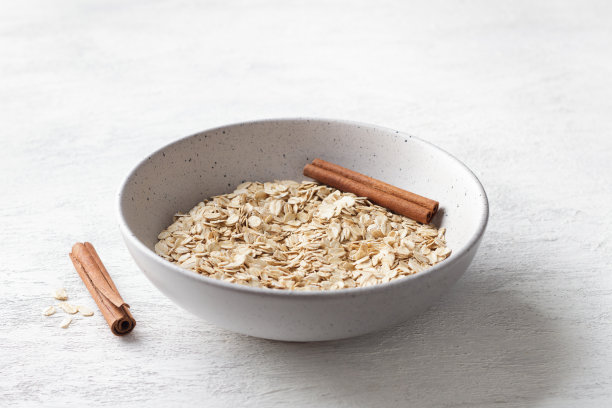 生燕麦片放在陶瓷碗里，浅灰色背景上有肉桂棒图片下载