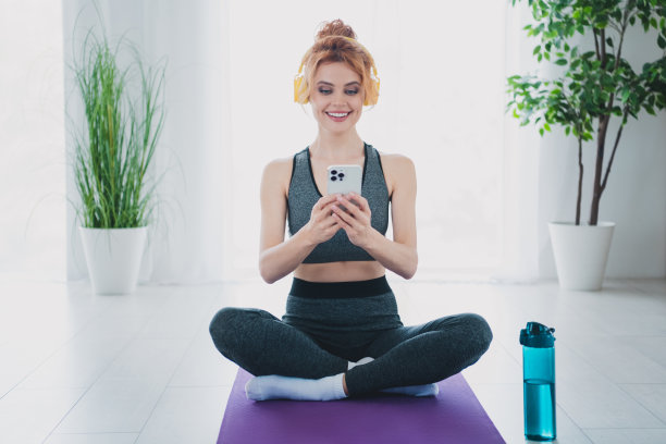 照片的运动活跃有吸引力的女人教练博主穿着运动服使用小工具手机健身房家庭房间日光室内图片下载