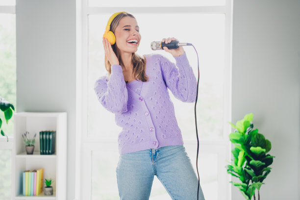 照片迷人的年轻女子耳机唱卡拉ok麦克风歌穿着紫色的衣服舒适的日光家室内客厅图片下载