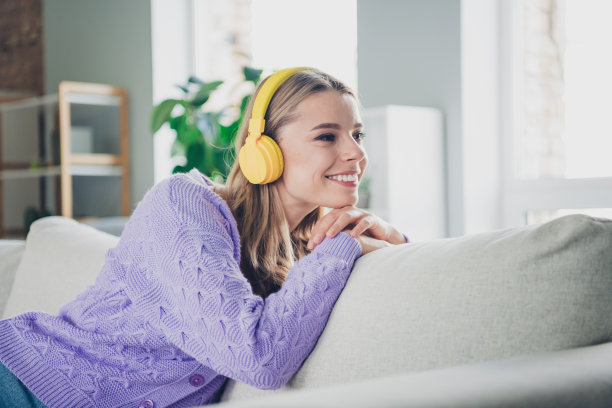 漂亮的年轻女孩的照片坐在沙发上耳机听音乐梦幻的看空空间穿紫色的衣服现代舒适的室内平坦的室内图片下载