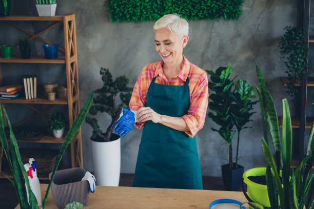 照片中，一个穿着围裙、戴着手套、在家里工作的快乐年龄段的女人正在收集植物图片下载