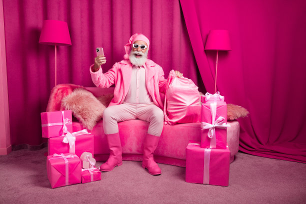 时髦帅气奢华的圣诞老人照片坐在沙发上用小玩意在房间粉红色的室内买圣诞礼盒图片下载