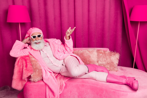 照片迷人的老人男友躺在沙发上粉红色的酒店房间室内穿靴子服装帽子太阳镜图片下载