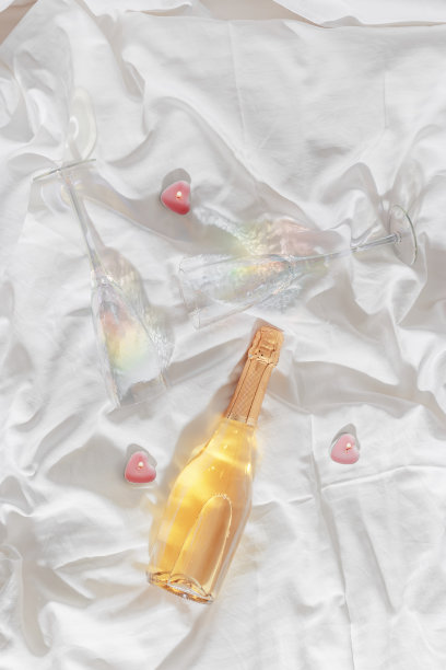 彩虹色闪闪发光的香槟酒杯，白色闪闪发光的酒瓶，白色床单上心形的粉色蜡烛。生活照片，明星滤镜。浪漫的聚会，浪漫的节日理念。图片下载