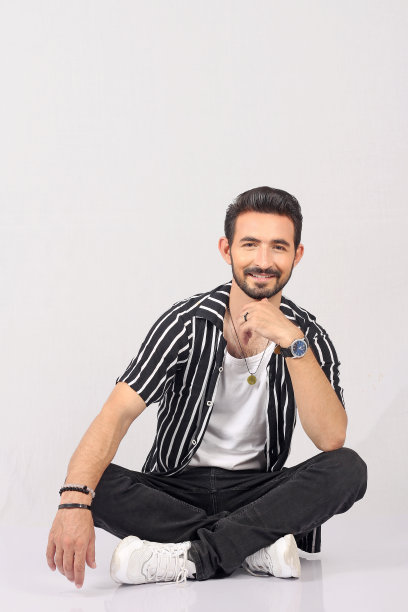 一个年轻的时尚男子的肖像在白色背景与黑色钮扣衬衫全高和坐着微笑的照片图片下载