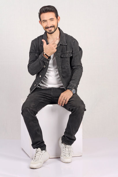 一个年轻的时尚男子的肖像在白色背景与黑色牛仔裤夹克全高和坐着的照片带着微笑图片下载