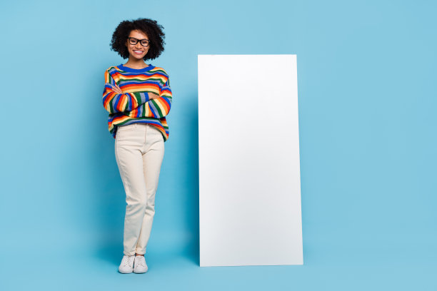 学生的全身照片卷发女士在电话附近戴眼镜衬衫牛仔裤运动鞋孤立的蓝色背景图片下载