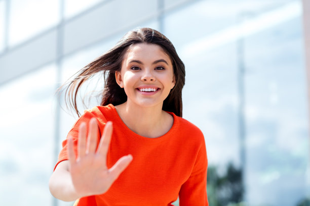 迷人的少女欢快的照片，女孩挥手，hi符号，与朋友见面，穿着红色的衣服在户外玩耍图片下载