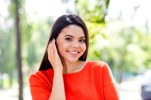 照片漂亮的青少年好心情的女孩掖头发在耳后迷人可爱害羞穿着红色的衣服走在城市公园外图片下载