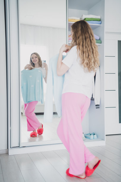 垂直全身照十几岁的金发女郎选择衣服镜子反射自拍照片穿着睡衣卧室白光室内图片下载