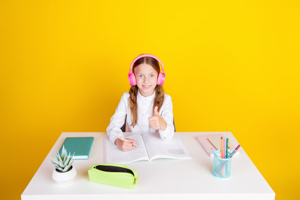 照片肖像可爱的小女生拇指向上听有声书作业穿着时尚的制服孤立在黄色的背景图片下载
