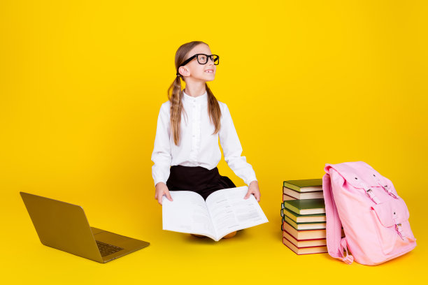 小女生网上课看书的全身照片看起来空空荡荡，穿着时尚的制服孤立在黄色的背景上图片下载