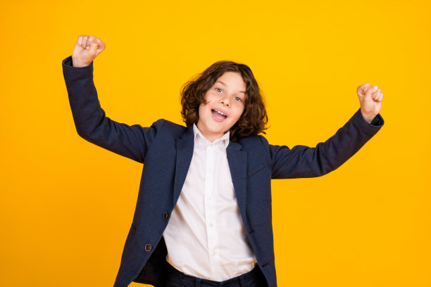 照片肖像的小男生举起拳头赢得穿着时尚的制服孤立的黄色背景图片下载