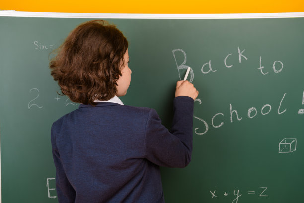 照片中可爱的男生穿着时髦的校服书写粉笔的教室黑板背景图片下载