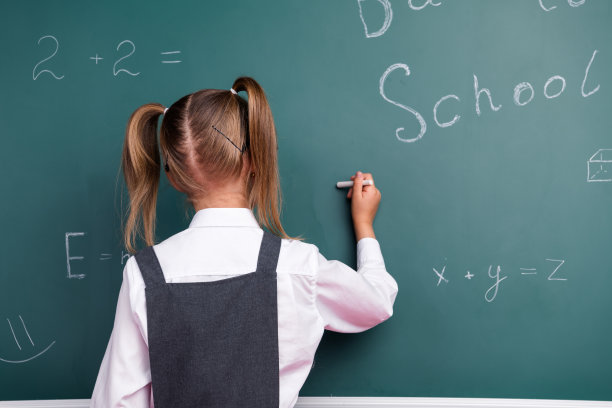 照片中迷人的小女生用粉笔答课，穿着时髦的校服教室黑板背景图片下载