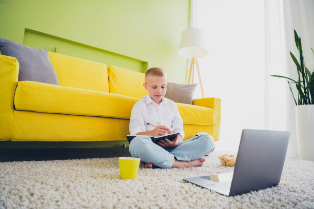 可爱可爱的男孩全身照片坐在地板上做作业上网本小学生远程课教育从家里在室内图片下载
