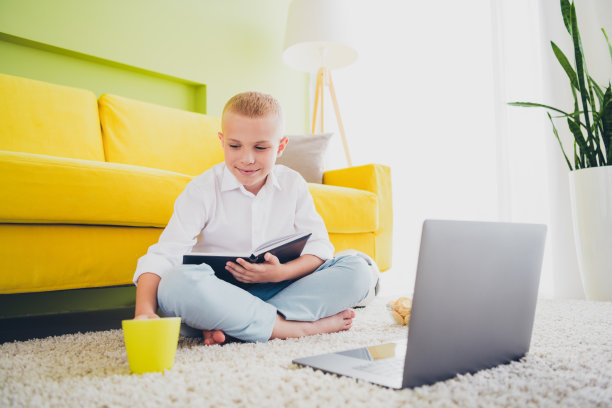 小可爱的儿子小学生的全尺寸照片坐在地板上喝茶做作业上网本远程教育家庭教育孤立的室内背景图片下载