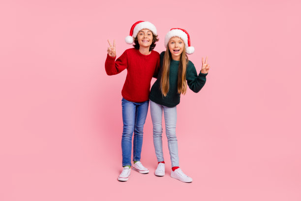 照片中的两个孩子，男孩，女孩看起来使v字形问候圣诞孤立的彩色背景图片下载