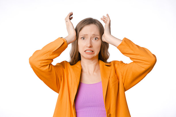 照片中的年轻女子震惊、害怕，看起来焦虑、担心，她站在白色的背景上，穿着橙色的运动夹克图片下载