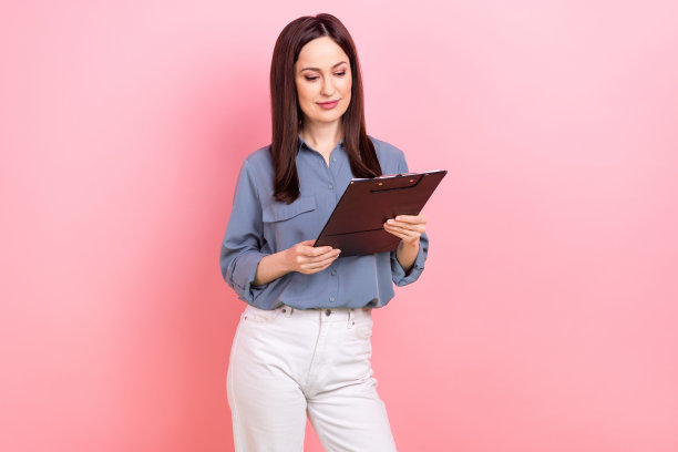 勤劳成功的女士穿着时髦的蓝色衣服，拿着粉红色背景上孤立的文件夹研究文件的照片图片下载