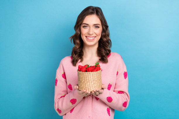 漂亮女孩的照片肖像拿着草莓篮子收获购物穿着时髦的粉红色印花衣服孤立的蓝色背景图片下载