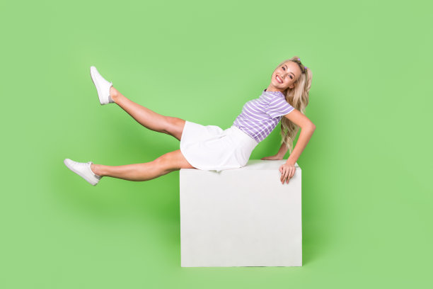 全身照片闪亮可爱的女士穿着紫色t恤坐在立方体平台孤立的绿色背景图片下载