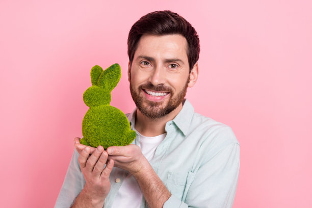 照片中英俊的年轻人抱着绿草兔兔可爱的身材，穿着时髦的蓝色衣服，孤立在粉红色的背景上图片下载