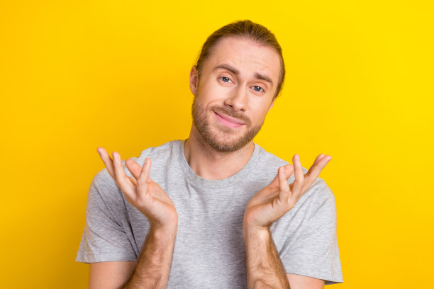 照片中，友好而困惑的英俊男子留着长发，穿着灰色t恤，手掌握在黄色背景上，毫无头绪图片下载