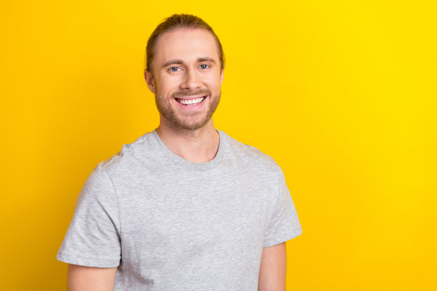 搞笑乐观的好心情男人的照片，留着长发，穿着灰色t恤，微笑的牙科广告孤立在黄色背景上图片下载