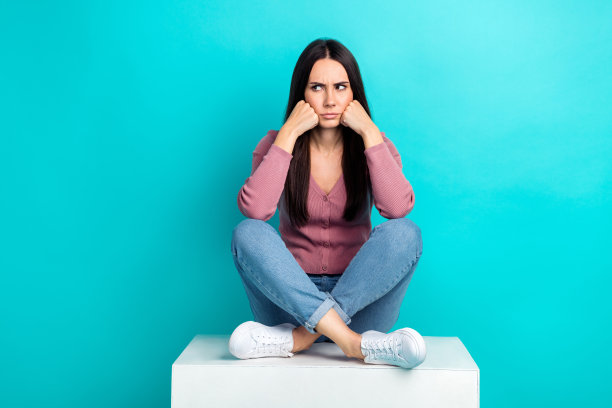 年轻的不快乐的侵略性的女人的全身尺寸的照片坐在立方体触摸脸颊看起来模拟冒犯孤立的海蓝宝石色背景图片下载