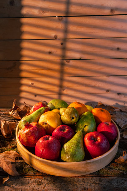 近距离拍摄的新鲜水果在木筐与水滴，秋叶和阳光在篮子和背景-股票照片图片下载