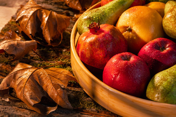 近距离拍摄的新鲜水果在木筐与水滴，秋叶和阳光在篮子和背景-股票照片图片下载