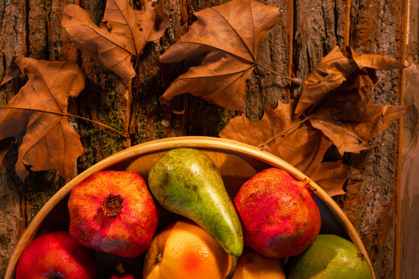 近距离拍摄的新鲜水果在木筐与水滴，秋叶和阳光在篮子和背景-股票照片图片下载