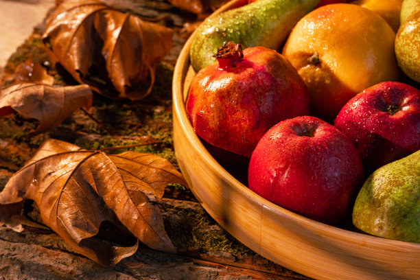 近距离拍摄的新鲜水果在木筐与水滴，秋叶和阳光在篮子和背景-股票照片图片下载