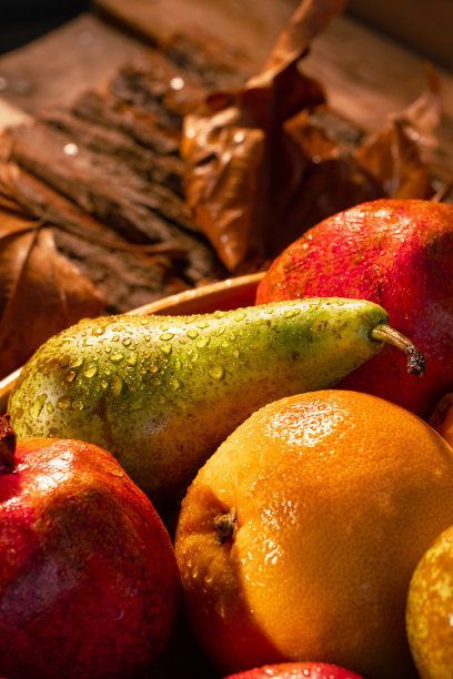 近距离拍摄的新鲜水果在木筐与水滴，秋叶和阳光在篮子和背景-股票照片图片下载