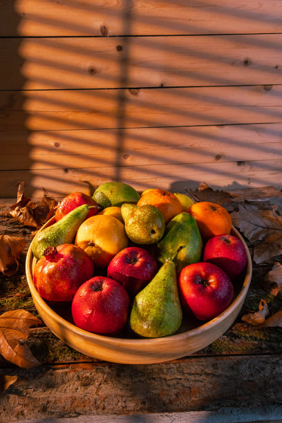 近距离拍摄的新鲜水果在木筐与水滴，秋叶和阳光在篮子和背景-股票照片图片下载