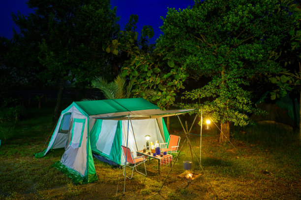 夜晚的露营帐篷，复古的小屋帐篷，古董灯笼，复古的椅子，以及森林里木制桌子上的户外咖啡制作设备图片下载