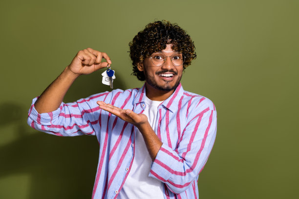 照片中，一个开朗的家伙留着波浪状的胡茬发型，穿着条纹衬衫，手臂上的钥匙被隔离在卡其色的背景上图片下载