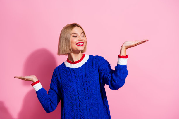 年轻微笑的金发波波头女孩的照片最终选择了产品在美容精品平衡手孤立在粉红色的背景图片下载