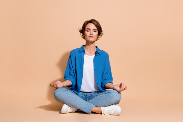 穿着蓝色衬衫的无忧无虑的年轻女子的全身照片，企业主在米色背景上平衡练习孤立图片下载