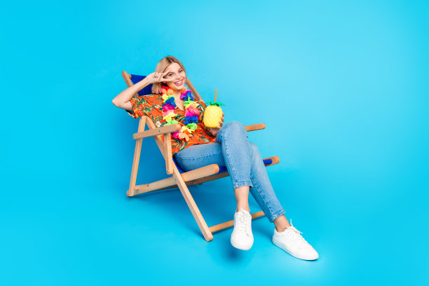 照片的开朗积极的女孩穿着时尚的印花衣服持有鸡尾酒v标志孤立的蓝色背景图片下载