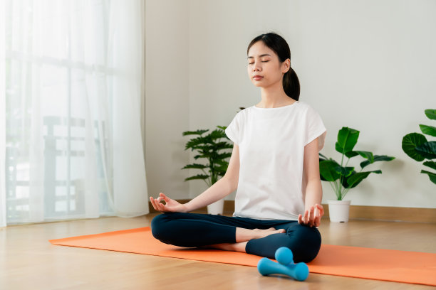 一个女人坐在地板上做莲花式，在家里练习瑜伽时冥想。图片下载
