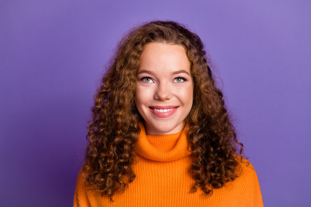 肖像照片卷曲的红头发年轻女子在橙色时尚的高领毛衣寻找copyspace孤立的紫罗兰色背景图片下载