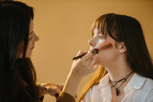 化妆师在摄影工作室用米色背景为女模特做准备图片下载