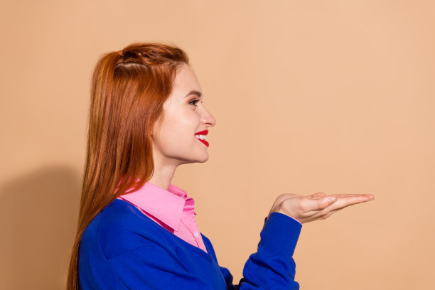 照片中心情愉快的女士穿着粉红色的衬衫，双手抱着空的空间，孤立的米色背景图片下载