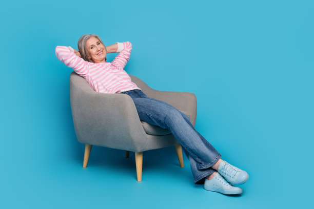 漂亮的高级女性的全身照片，坐在扶手椅上，双手放在头后，穿着时髦的条纹服装，孤立在蓝色背景上图片下载