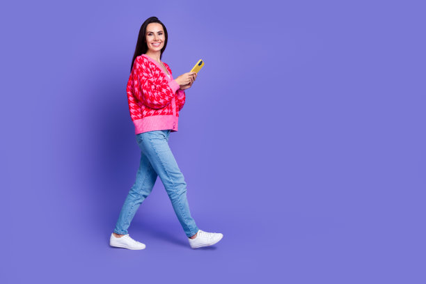 迷人的积极的女人穿着粉红色的开襟毛衣阅读现代小工具走空空间孤立的紫色背景的全长照片图片下载