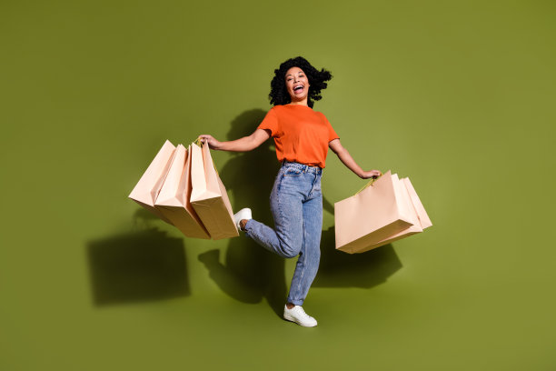 漂亮的年轻女子拿着购物袋的全尺寸照片，穿着卡其色背景上孤立的t恤图片下载